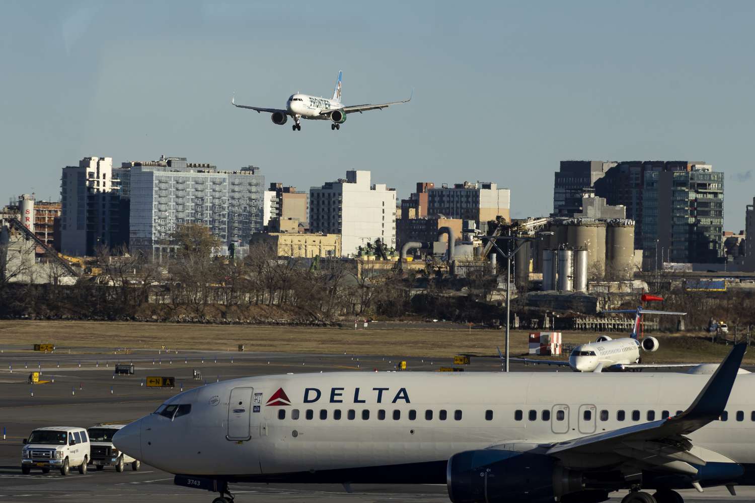 A Delta plane sits on a runway below a plane coming in for a landing 