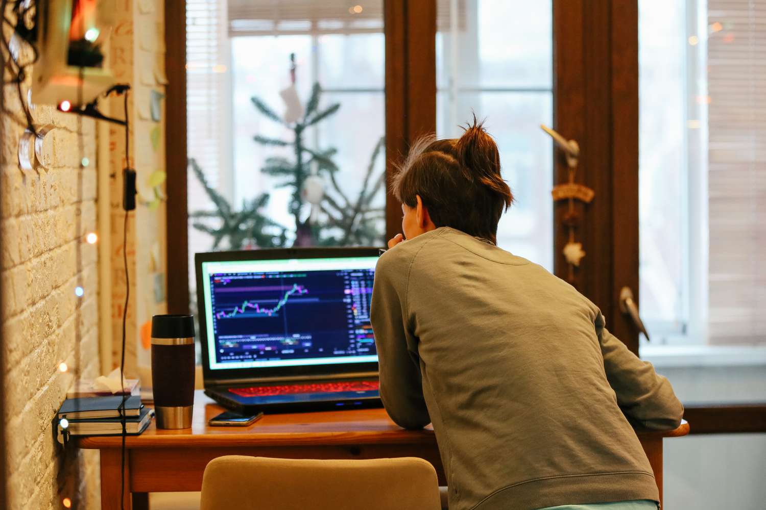 Back view of woman sitting at a desk studying a chart and other data on a computer.
