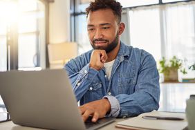 a person sitting in an office in front of a laptop looking intently at the screen 