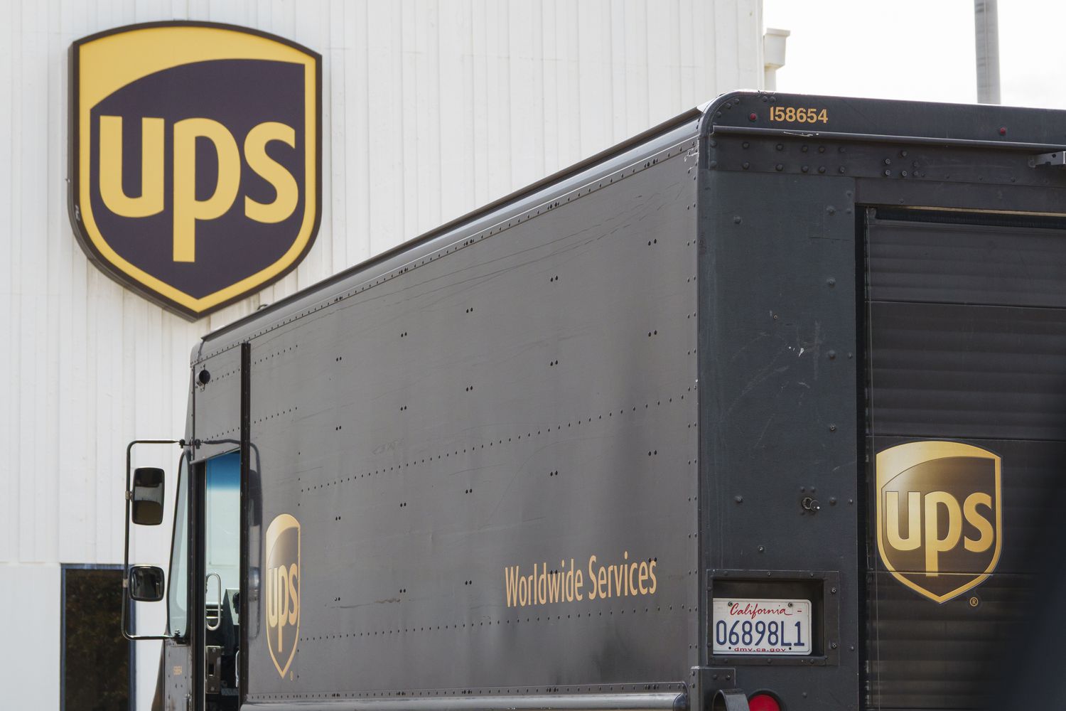 The UPS logo is seen on the side of a building, with a brown UPS van in front of it.