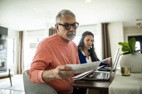 Two individuals reviewing documents at a desk with a laptop