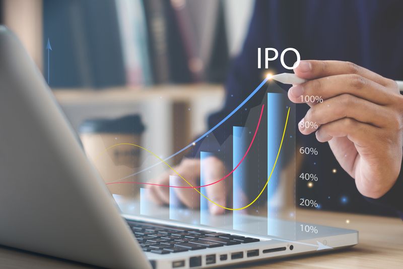 A close up of a laptop and a hand holding a pen pointing to a graphic of the rising price of an initial public offering.