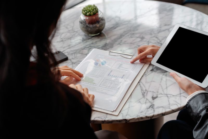 People discussing a balance sheet. One is holding a tablet while pointing to a document.