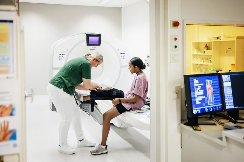 A CT technician assists a patient with her leg brace before she lies down for a scan.