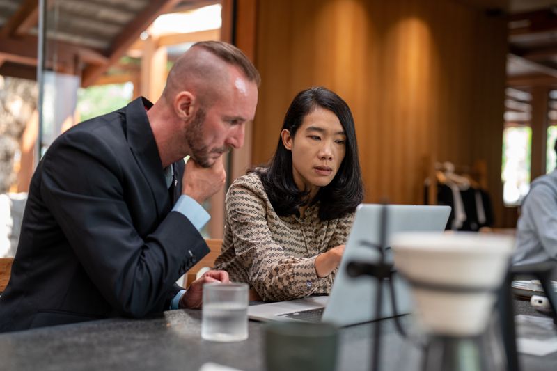 A couple sits in a cafe while looking at laptop to track the Zacks Lifecycle Index of their target-date retirement investment.