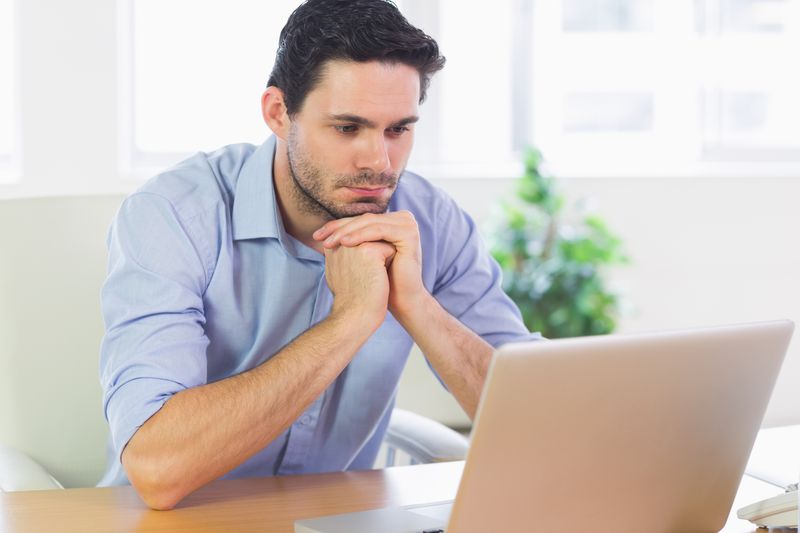 Young man sitting at a table and looking seriously at something on his laptop