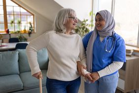Young woman home caregiver assisting a woman in her home as she uses a cane. 