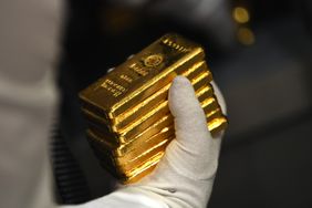 Gloved hand holding several bars of gold.