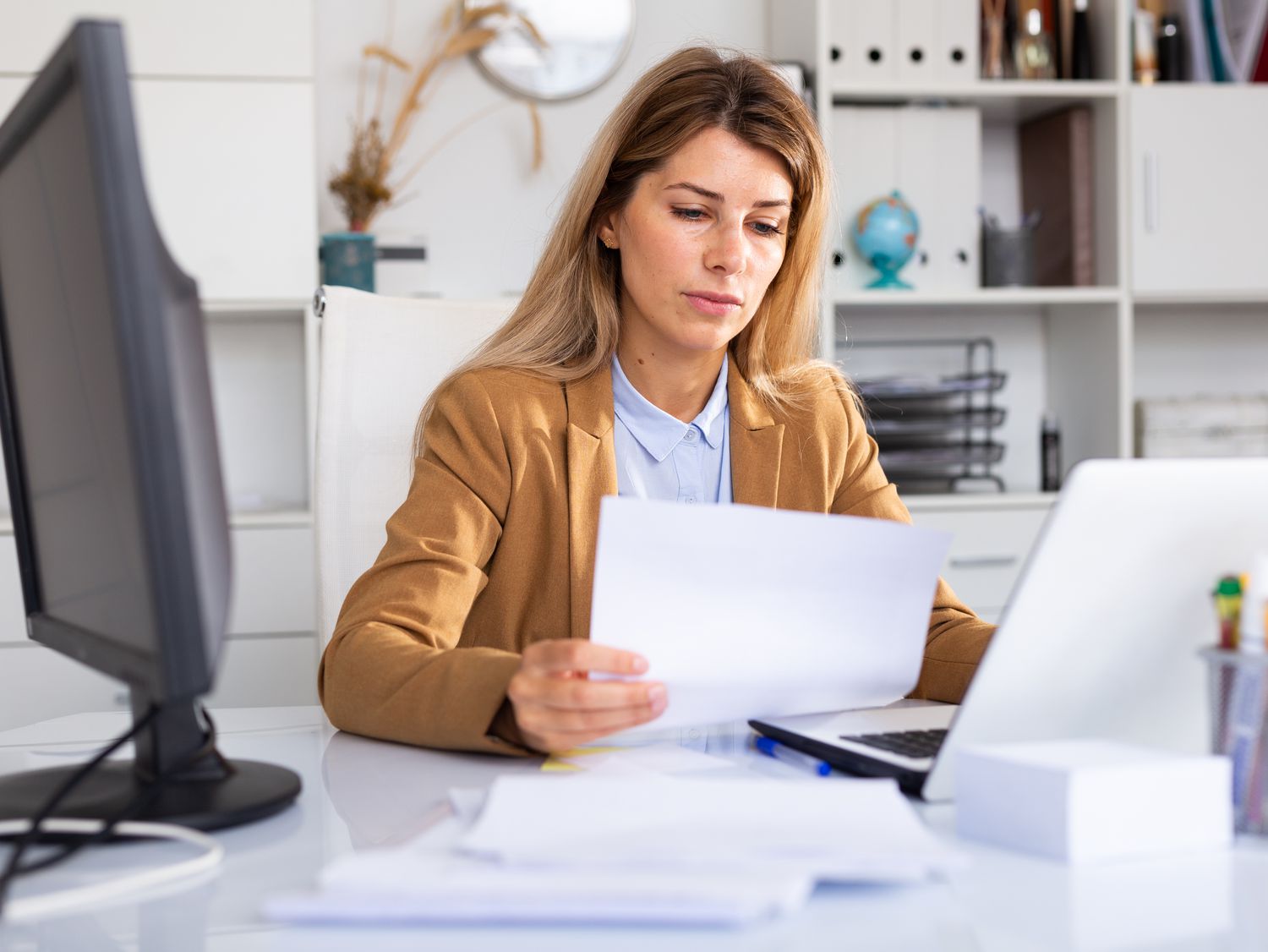 Woman sitting at home desk and looking at bank statements and a laptop