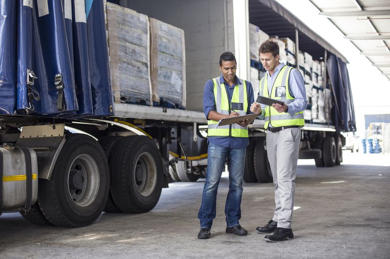 two workers looking at clipboards with a loaded truck behind them