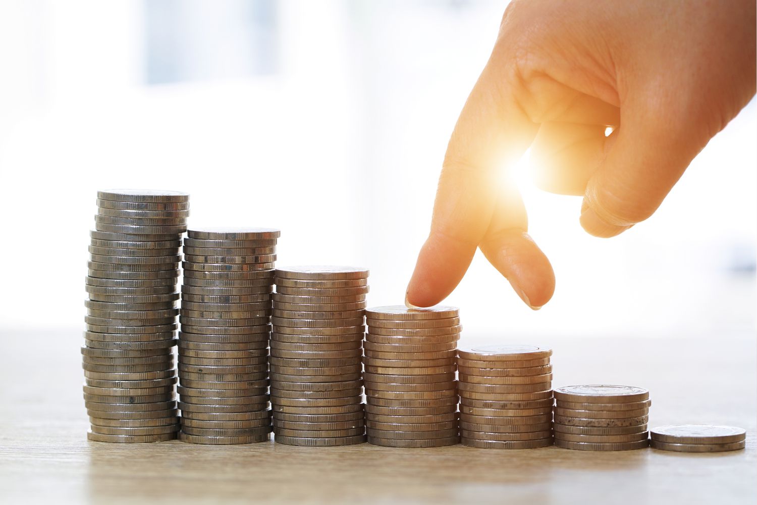 A stack of coins displayed in a decreasing way with a hand walking on it.