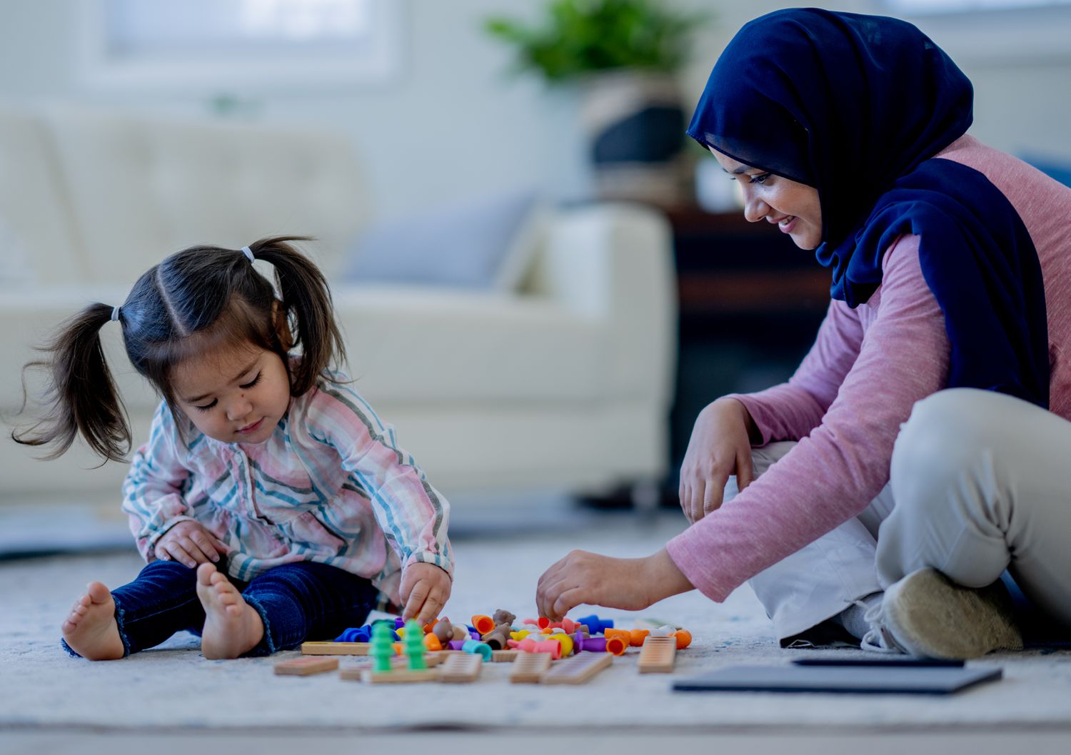 A woman sits on the floor with a little girl. 