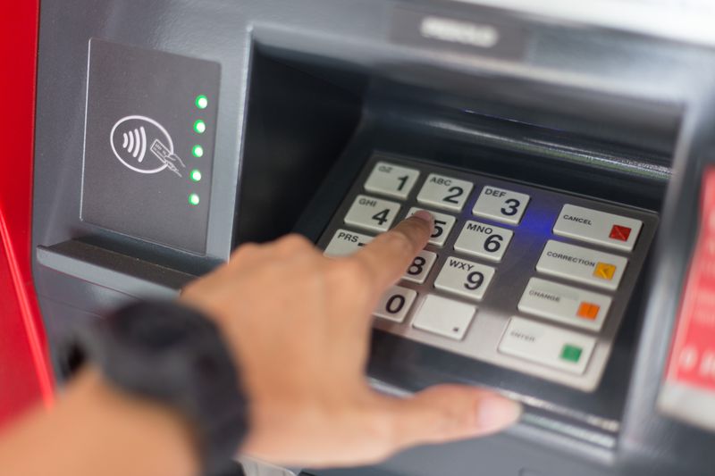 Hand entering PIN code at ATM machine.