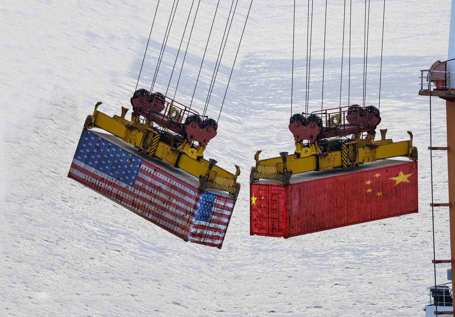 Two containers being moved over water. One is wrapped in the colors of the American flag. The other wrapped in the Chinese flag. 