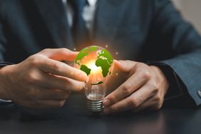 A businessperson holds a light bulb featuring a green Earth to represent sustainability and environmental responsibility in the modern world.