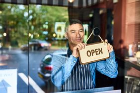 Small business owner holding an "open" sign inside the business