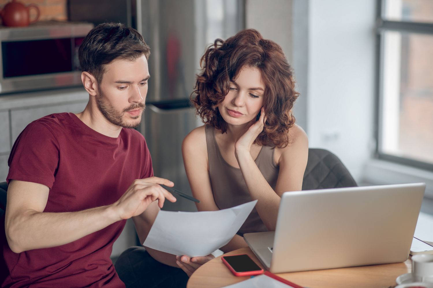 Young couple sitting at their kitchen table an looking together at documents and a laptop