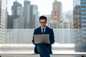 Man sitting outside working on a laptop resting on his lap. 