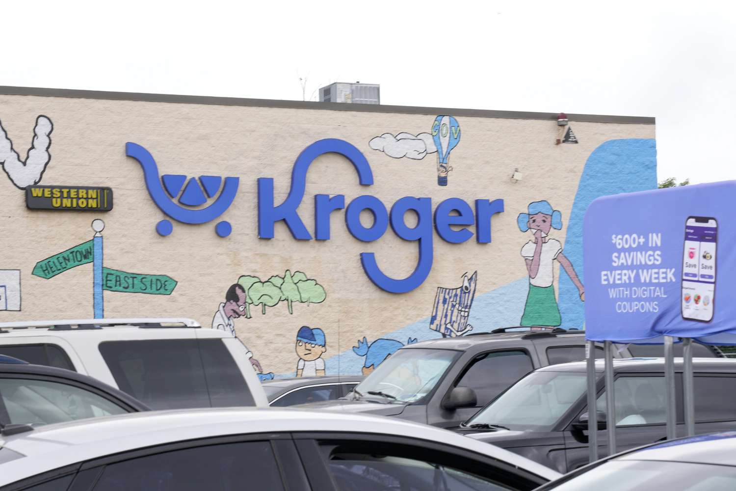 Cars are parked in front of a Kroger store with art surrounding the blue Kroger logo.