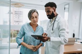 Doctor talking to gray-haired patient and showing her something on a tablet computer