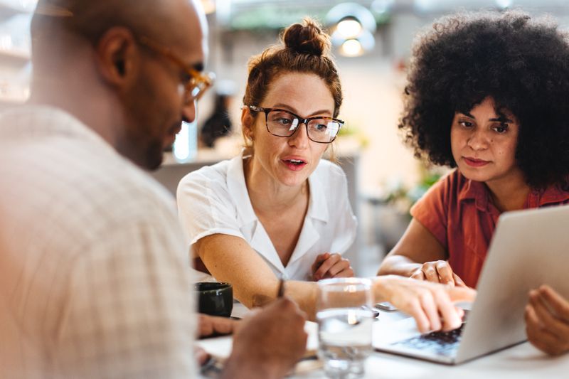 Three business people sitting round a table discussing something on a laptop