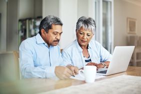 Older couple sitting at their dining table and looking together at mortgage documents and rates on a laptop