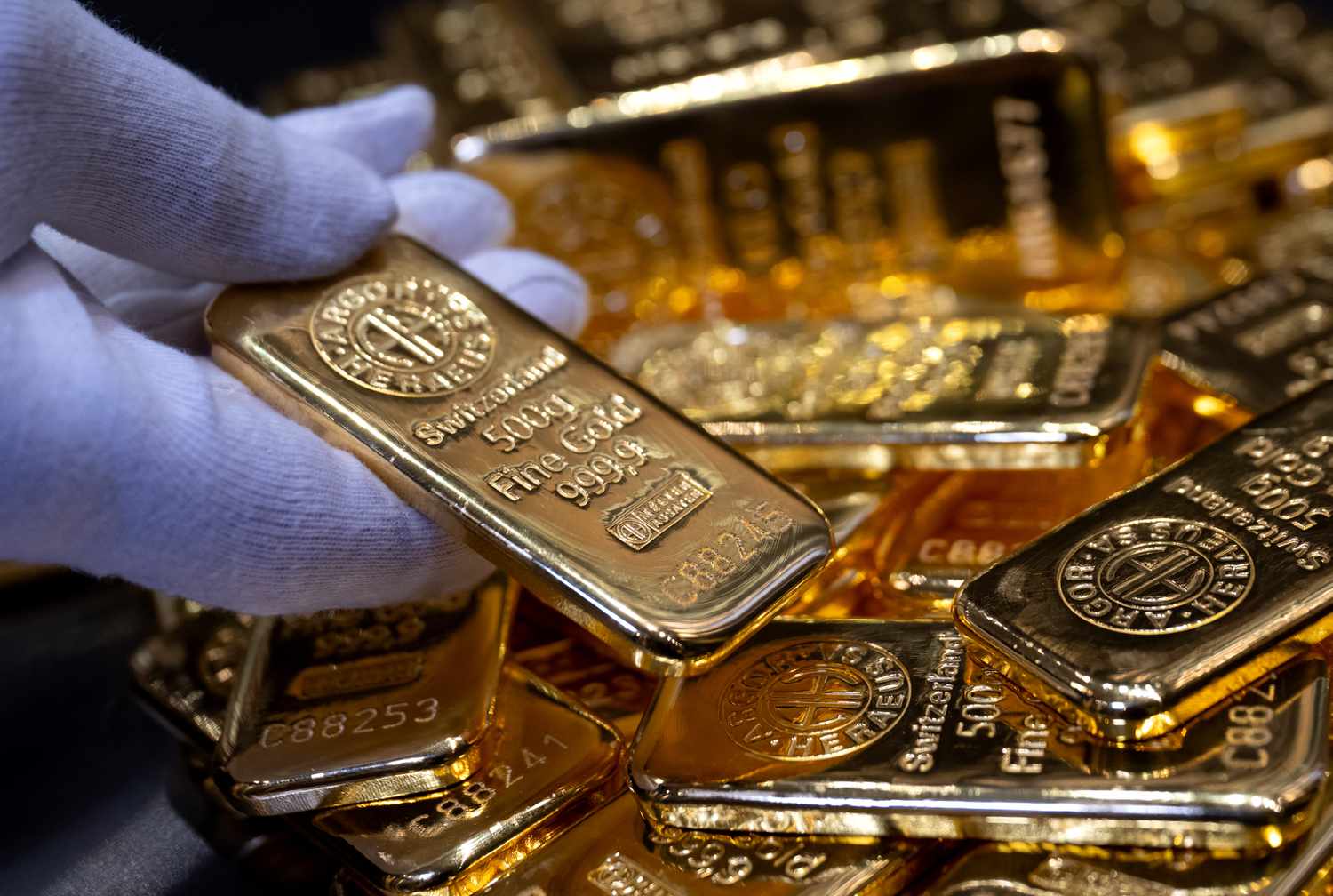 A gloved hand holding a gold bar among several others