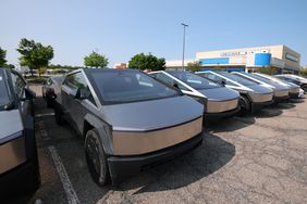 A row of Tesla Cybertrucks in a parking lot, with blue sky and a building in the background