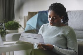 Young woman reading a paycheck statement while sitting on the floor leaning on her couch