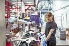 Female worker working with cobot, a collaborative robot, in robotic assembly machine in automotive parts factory