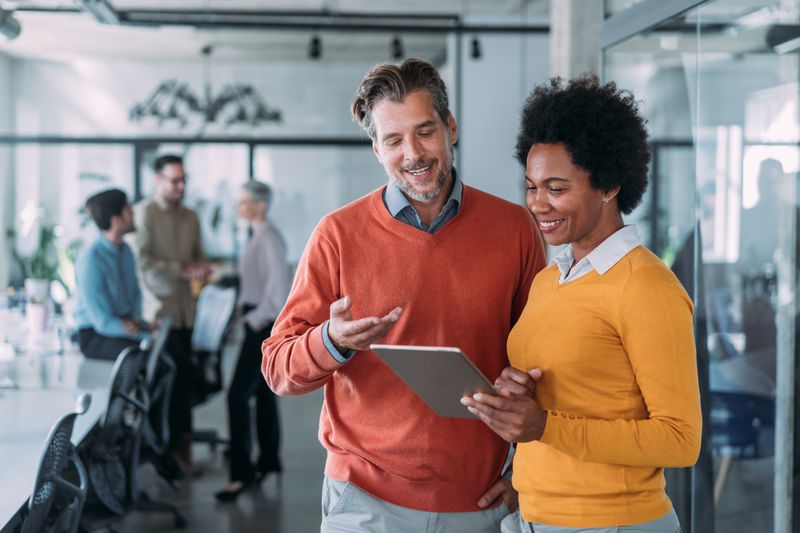 Image shows two investors having a discussion while view a mobile device. 