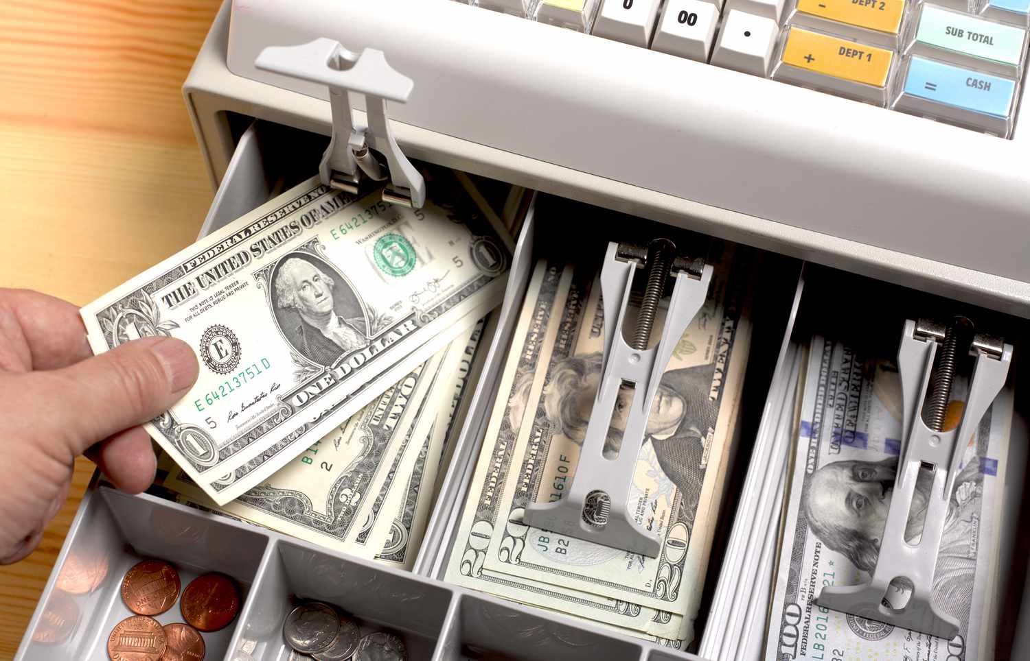 close up shot of the open drawer of a cash till, full of American dollars, with a person putting a $1 bill in.