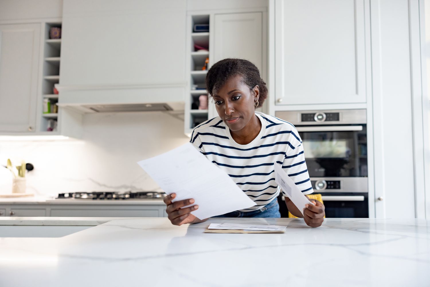 A woman stands at a kitchen island looking at paperwork