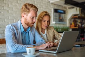 Couple in their 20s or 30s sitting in a coffee shop and looking at online mortgage rates