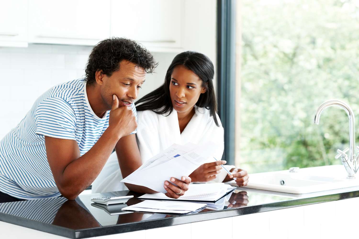 A worried couple look at financial documents in their kitchen.