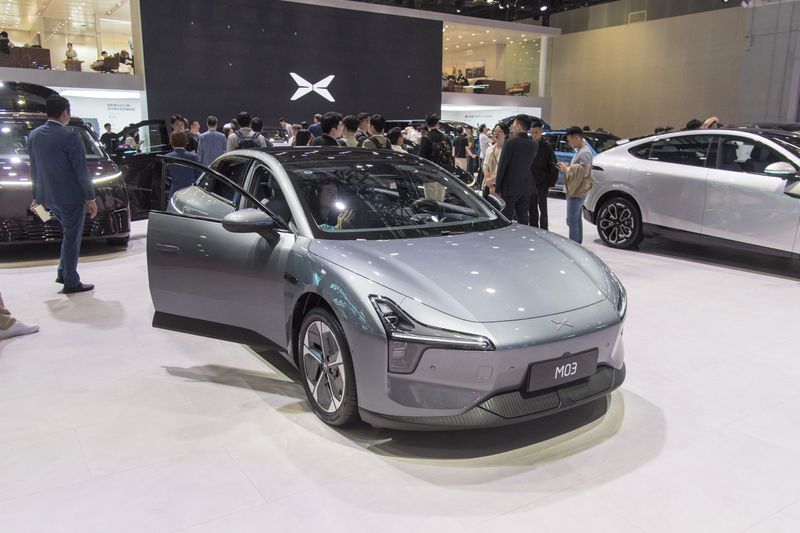 People are seen gathered around several cars, with the XPeng logo visible on a wall in the background.