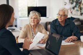 Woman talking to senior couple with paperwork in hand and a laptop in front of her. 