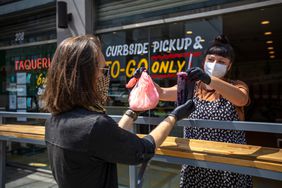Masked restaurant worker and customer picking up food curbside during the COVID-19 pandemic.