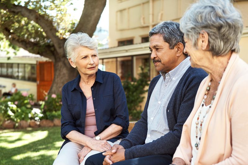 Shot of a group of older friends sitting together on a bench out in a community garden.