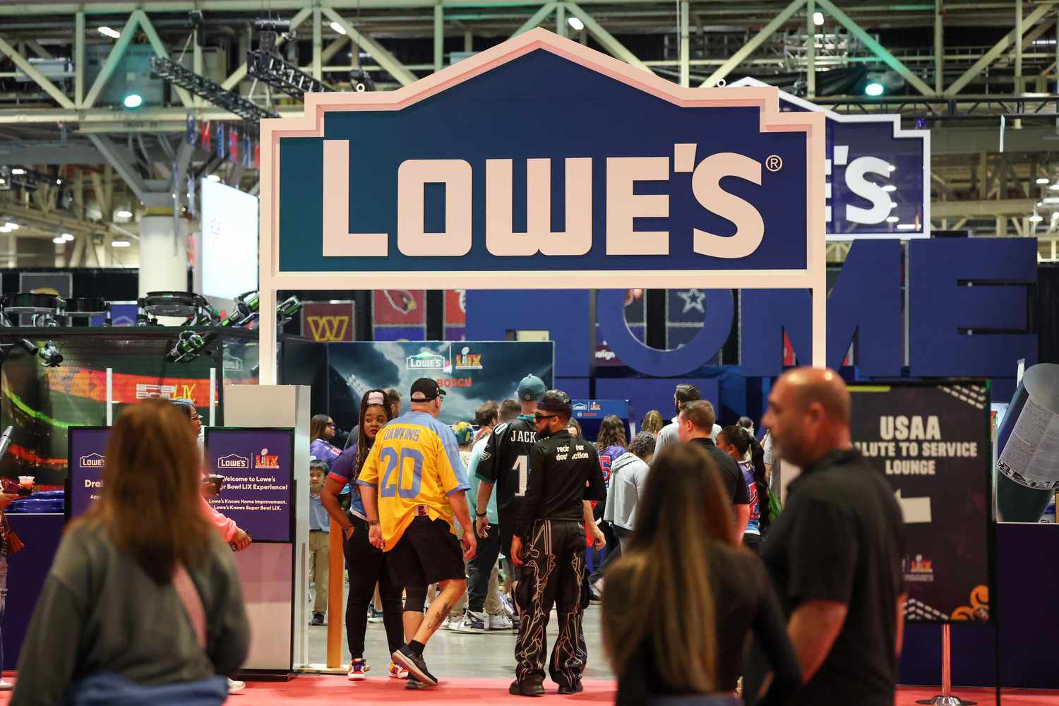 People walk through the entrance to a Lowe's section of a Super Bowl event, with the blue and white Lowe's logo above the entrance.