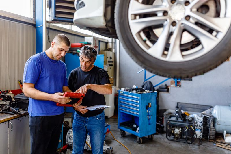 A car maintenance worker consults with male customer about a car that is raised up next to them.
