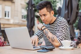 A person focusing on a laptop while seated at an outdoor table