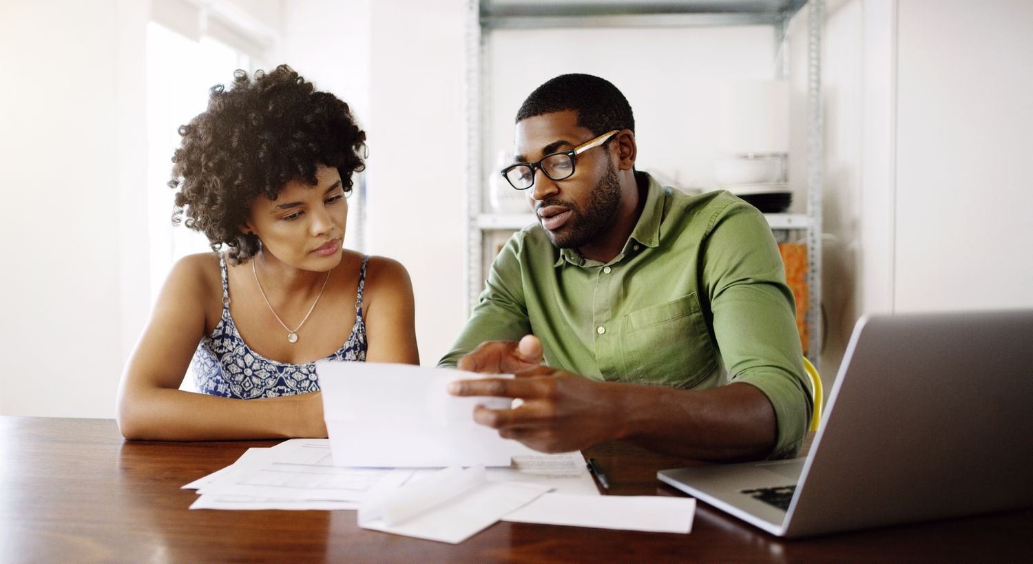 Young couple sitting at their dining room table and looking at mortgage documents and a laptop
