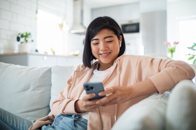 Close up of a young woman using a smart phone while sitting on a couch in a living room