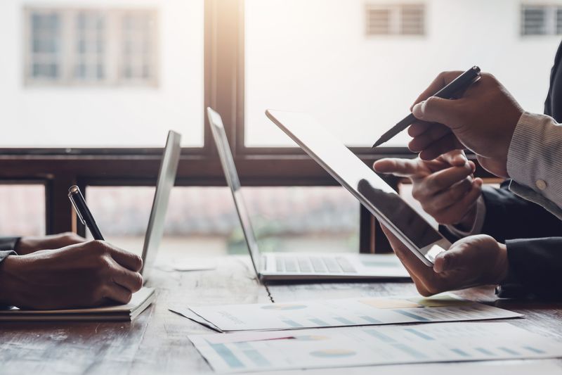 Cropped hands of business people in a meeting using tablets with financial papers on the table