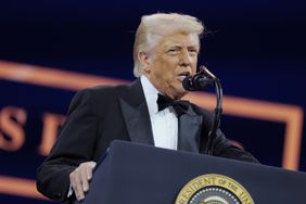 Donald Trump speaks in a black tuxedo in front of a podium and microphone