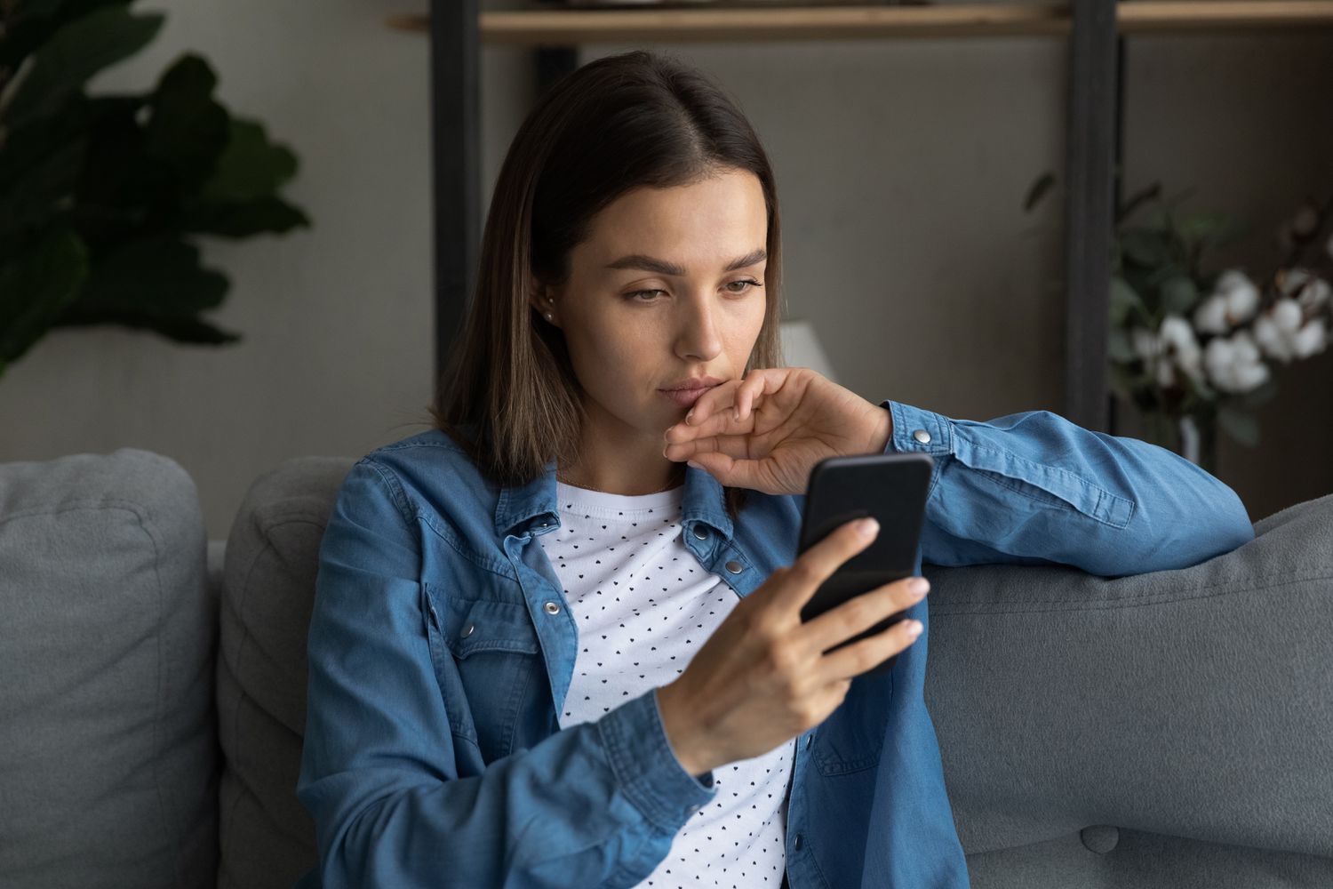 Young woman sitting on her sofa and looking at something on her smartphone