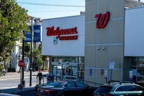 People and cars are seen on the street in front of a Walgreens pharmacy store.
