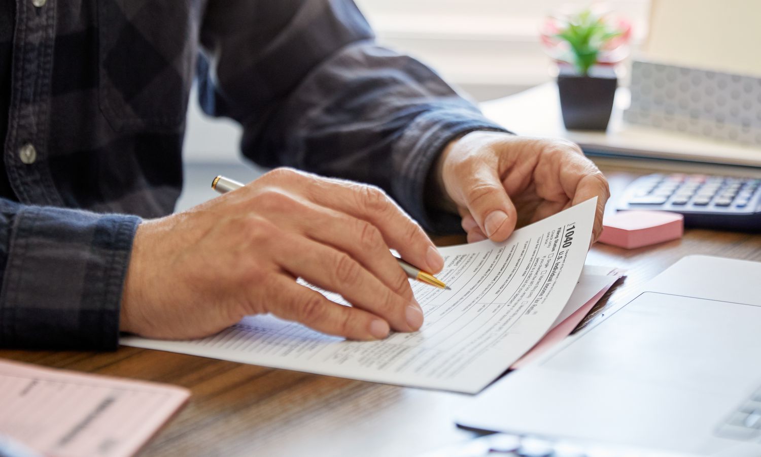 A close-up of a man's hands holding a pen and a tax form while sitting at a desk