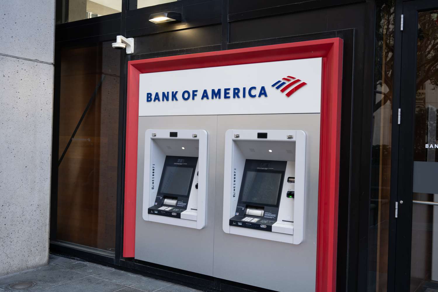 The Bank of America logo is seen above two ATMs on the street.